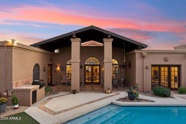 6208 E Paradise Ln, Scottsdale, AZ 85254 - back of property at dusk with a patio, stucco siding, an outdoor kitchen, an outdoor pool, and french doors