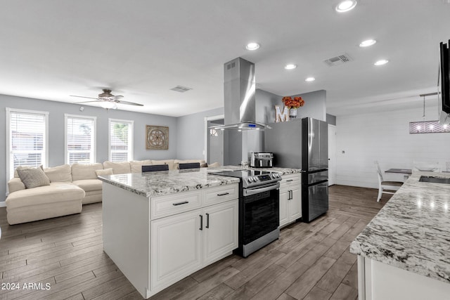 kitchen with light stone counters, white cabinets, island range hood, appliances with stainless steel finishes, and ceiling fan