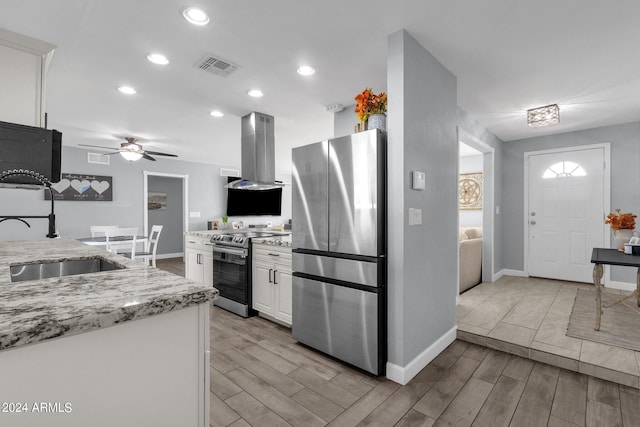 kitchen featuring appliances with stainless steel finishes, light hardwood / wood-style floors, light stone counters, island exhaust hood, and ceiling fan