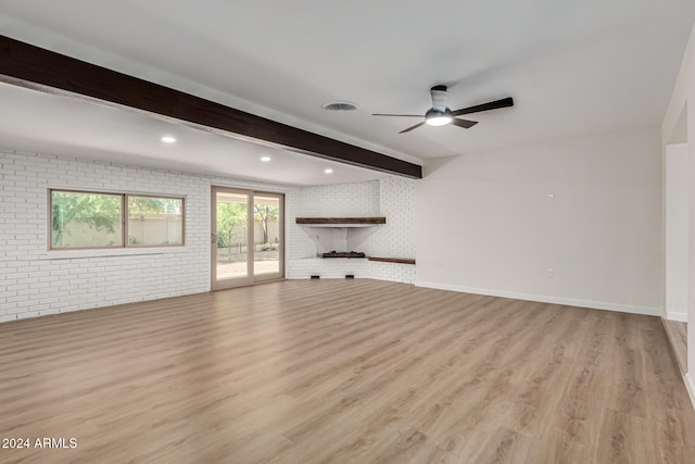 unfurnished living room featuring ceiling fan, light wood-type flooring, a fireplace, beamed ceiling, and brick wall