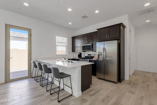 3885 E Kenley Ln, San Tan Valley, AZ 85143 - kitchen with stainless steel appliances, a sink, a breakfast bar area, dark brown cabinetry, and light wood-style flooring