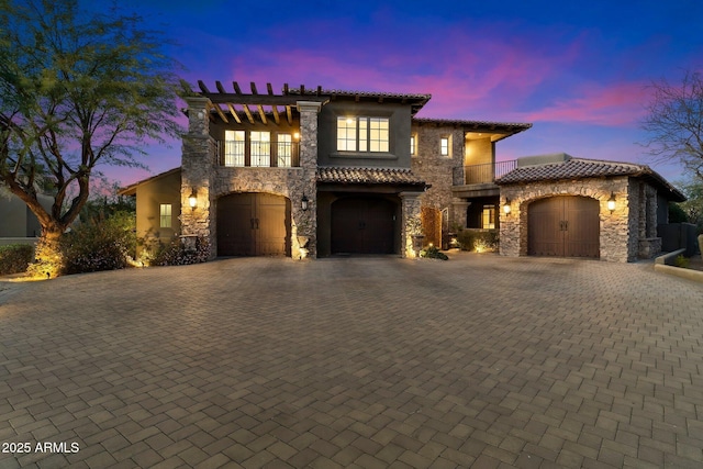 mediterranean / spanish-style house with a balcony, stone siding, a tile roof, decorative driveway, and stucco siding