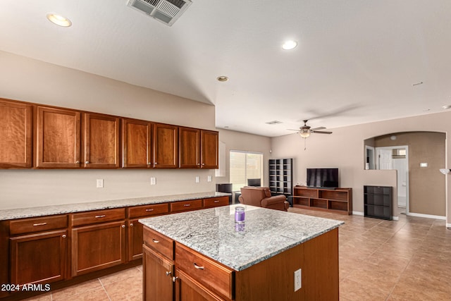 kitchen featuring ceiling fan, a center island, and light stone countertops