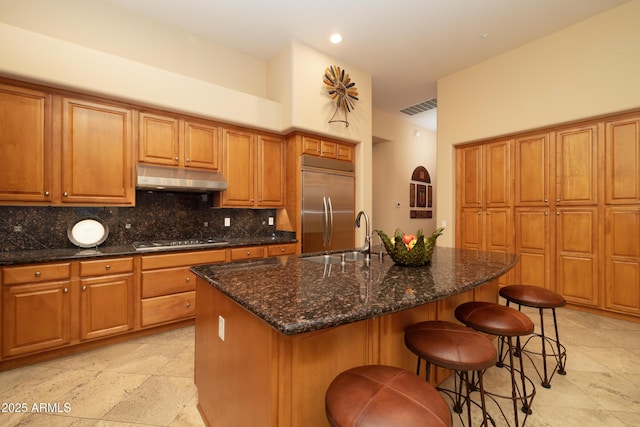 kitchen featuring gas stovetop, visible vents, stainless steel built in fridge, a sink, and under cabinet range hood