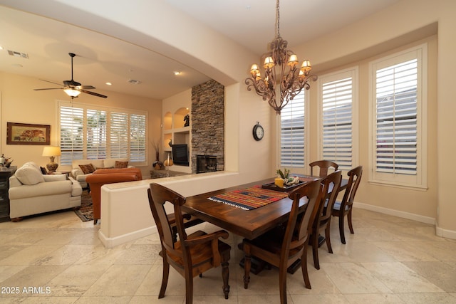 dining space featuring arched walkways, visible vents, a stone fireplace, baseboards, and ceiling fan with notable chandelier