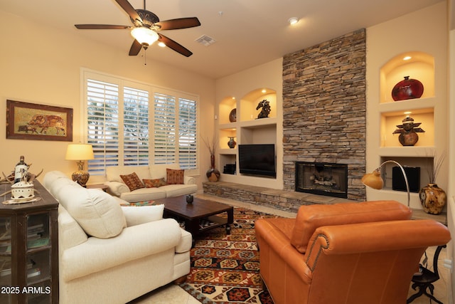 living room with built in shelves, a fireplace, visible vents, and a ceiling fan