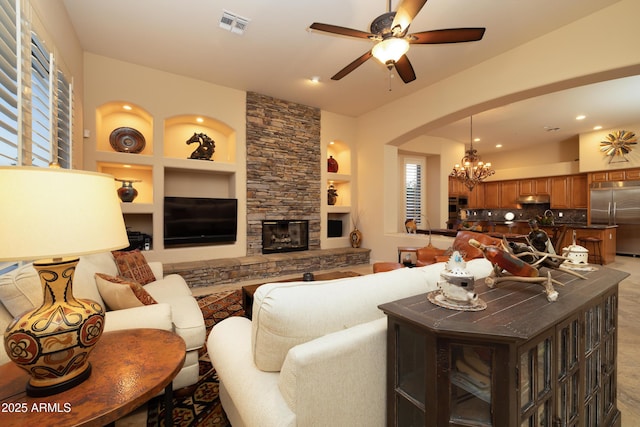 living room with visible vents, built in features, ceiling fan with notable chandelier, a stone fireplace, and recessed lighting