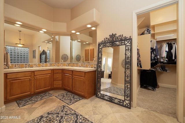 full bathroom featuring double vanity, a sink, a walk in closet, and baseboards