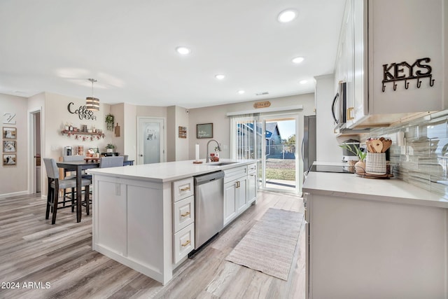 kitchen featuring sink, hanging light fixtures, stainless steel appliances, a center island with sink, and white cabinets