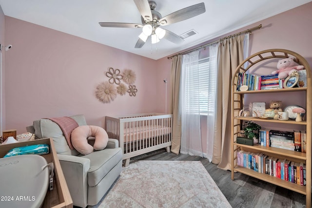 bedroom featuring hardwood / wood-style floors, ceiling fan, and a nursery area