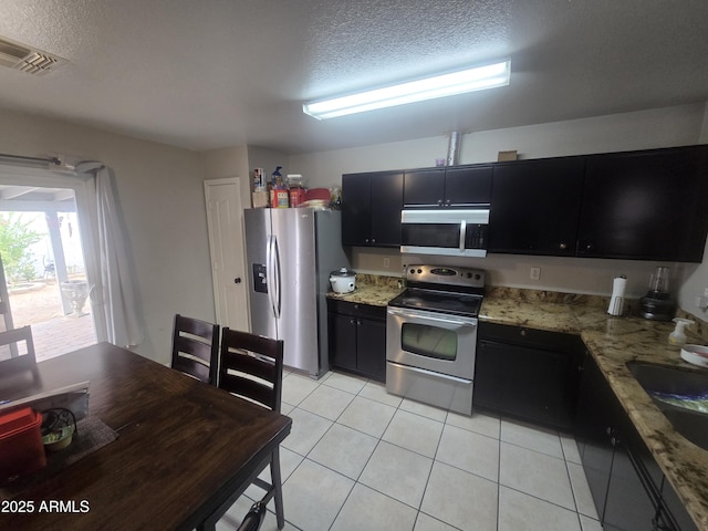 11770 W Aster Dr, El Mirage, AZ 85335 - kitchen featuring stainless steel appliances, dark cabinets, a textured ceiling, light tile patterned floors, and light stone counters