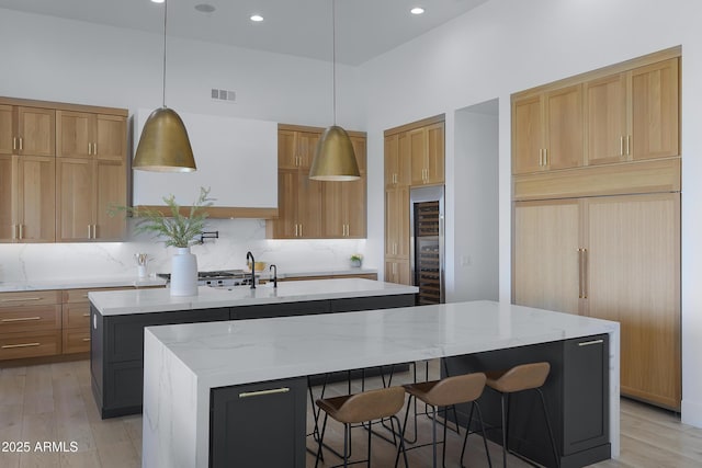 kitchen with decorative backsplash, light wood-style floors, a kitchen island with sink, and visible vents