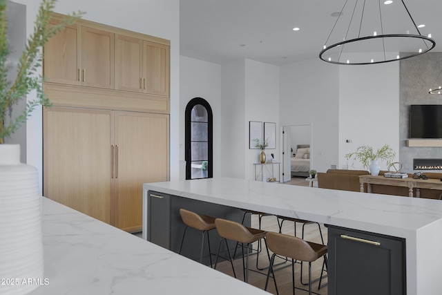 kitchen featuring light stone countertops, a kitchen breakfast bar, light brown cabinetry, a high ceiling, and open floor plan