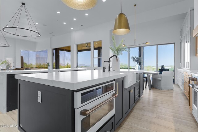 kitchen featuring dark cabinets, recessed lighting, light wood-style floors, a large island with sink, and a sink