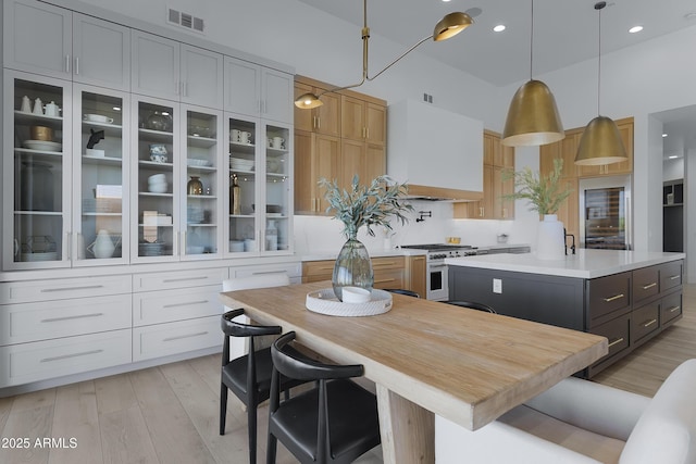 kitchen with gas stove, glass insert cabinets, light countertops, light wood-style flooring, and visible vents