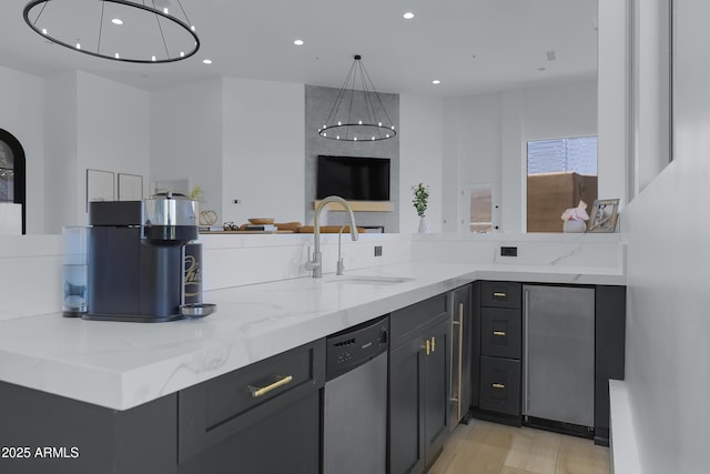 kitchen featuring stainless steel dishwasher, light stone countertops, light wood-style flooring, a sink, and open floor plan