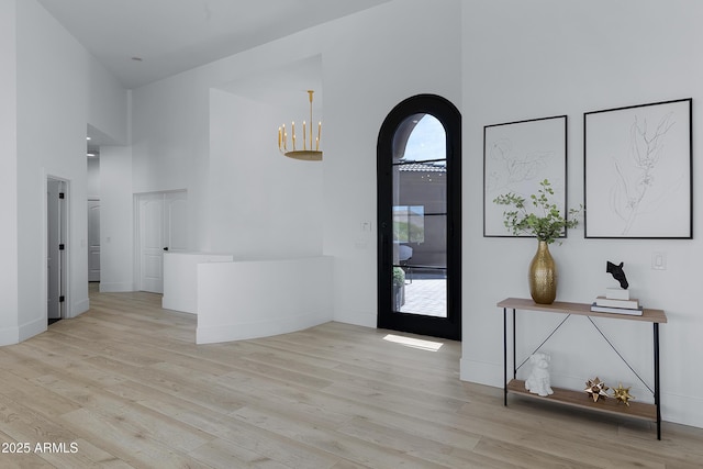 entrance foyer featuring arched walkways, baseboards, a towering ceiling, and wood finished floors