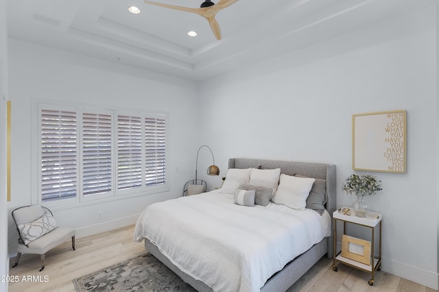 bedroom featuring recessed lighting, a tray ceiling, baseboards, and wood finished floors
