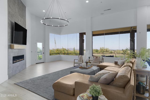 living room with visible vents, recessed lighting, a towering ceiling, ceiling fan with notable chandelier, and a large fireplace