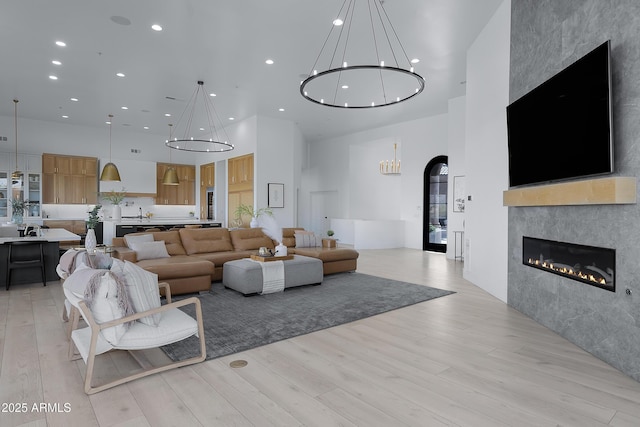 living area with a chandelier, recessed lighting, light wood finished floors, and a towering ceiling