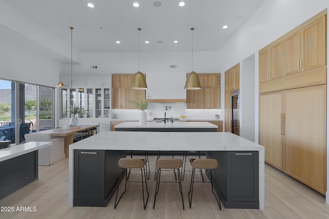 kitchen with recessed lighting, a high ceiling, light wood finished floors, light brown cabinets, and a spacious island