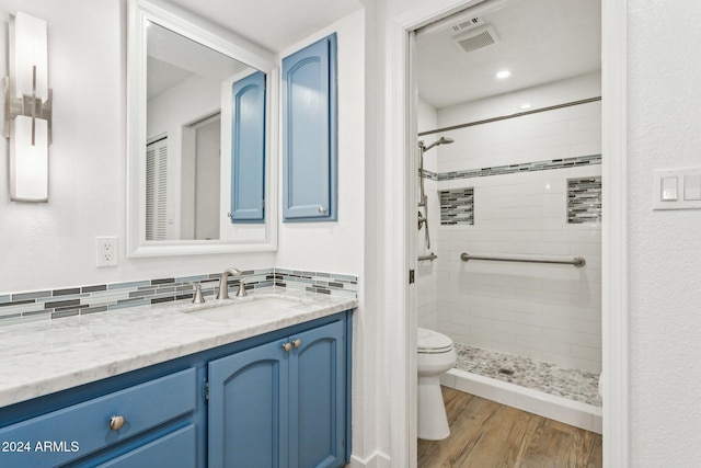 bathroom featuring a tile shower, hardwood / wood-style floors, toilet, decorative backsplash, and vanity