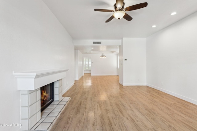 unfurnished living room featuring ceiling fan, a tiled fireplace, and light hardwood / wood-style flooring