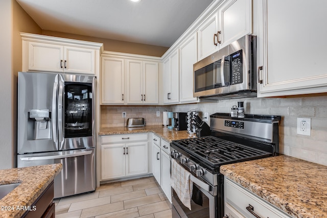 kitchen with decorative backsplash, light stone counters, white cabinetry, and stainless steel appliances