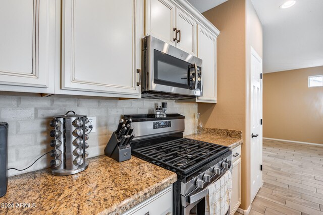 kitchen featuring white cabinetry, light stone counters, stainless steel appliances, and light wood-type flooring