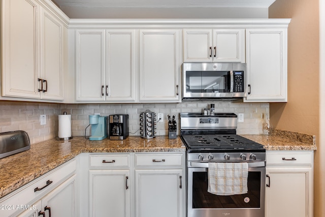 kitchen with decorative backsplash, white cabinets, and appliances with stainless steel finishes