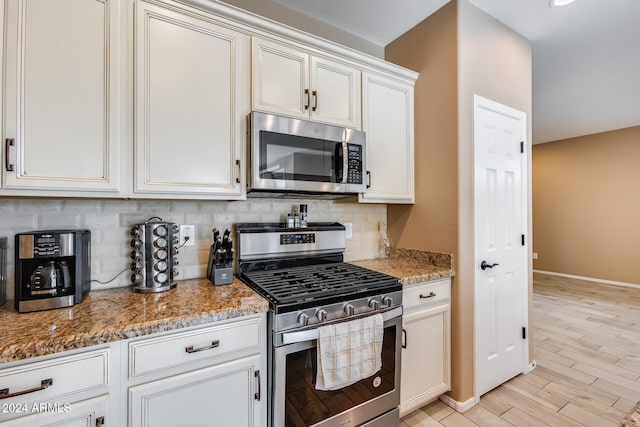 kitchen with dark stone counters, white cabinets, tasteful backsplash, light hardwood / wood-style floors, and stainless steel appliances