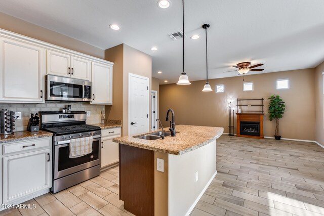 kitchen featuring white cabinets, decorative light fixtures, stainless steel appliances, and a center island with sink