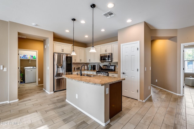 kitchen with backsplash, stainless steel appliances, sink, decorative light fixtures, and an island with sink