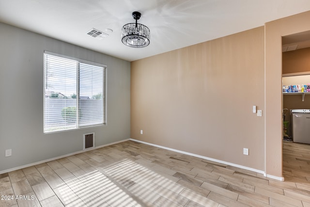 empty room with washer / dryer, light wood-type flooring, and a notable chandelier