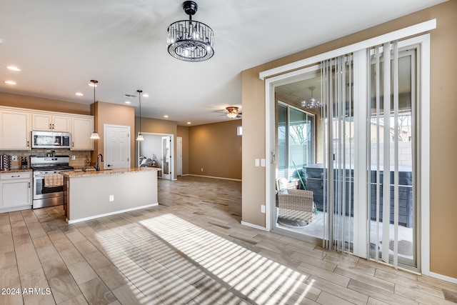 kitchen with white cabinetry, hanging light fixtures, stainless steel appliances, decorative backsplash, and a center island with sink