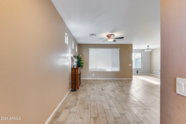 empty room featuring ceiling fan with notable chandelier and light hardwood / wood-style flooring