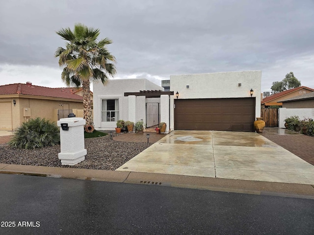 pueblo-style house featuring driveway, an attached garage, fence, and stucco siding