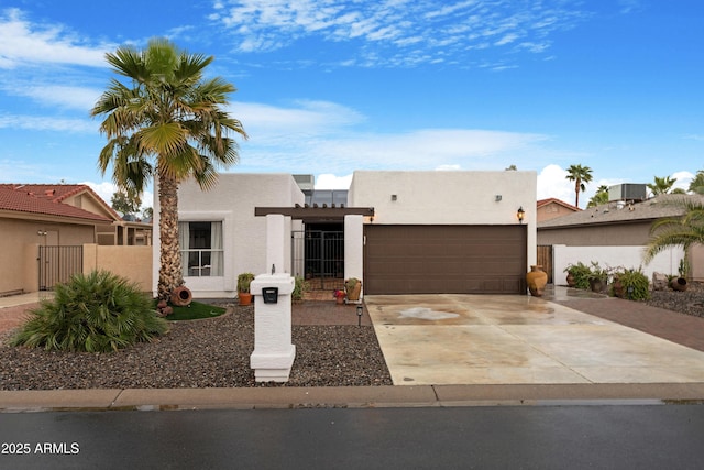 pueblo revival-style home featuring driveway, an attached garage, a gate, fence, and stucco siding