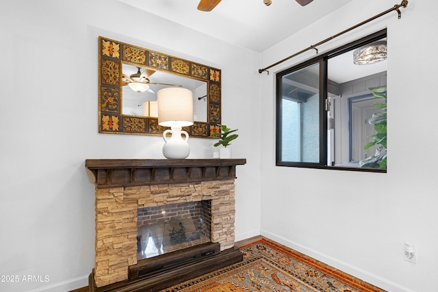 unfurnished living room featuring ceiling fan, a stone fireplace, wood finished floors, and baseboards