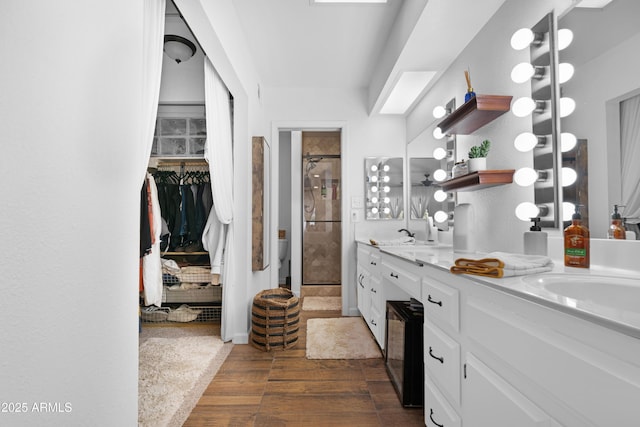 bathroom featuring a sink, wood finished floors, a shower stall, double vanity, and a walk in closet