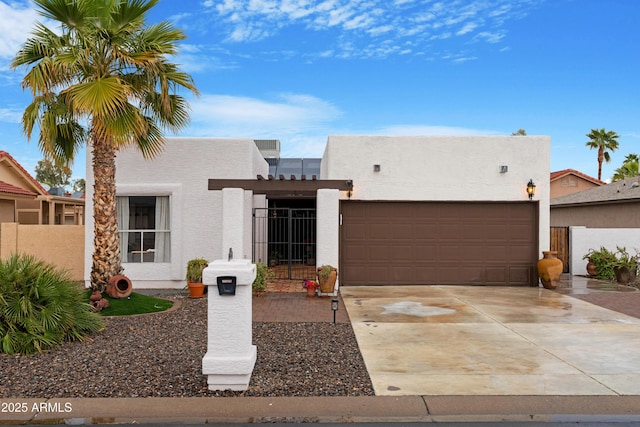 adobe home with an attached garage, driveway, fence, and stucco siding