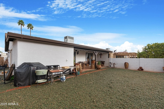 back of house with stucco siding, fence, a lawn, and a patio