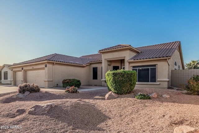 mediterranean / spanish home with stucco siding, driveway, an attached garage, a tiled roof, and fence