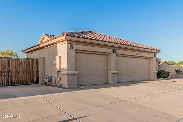 view of home's exterior with driveway, stucco siding, a tiled roof, and fence
