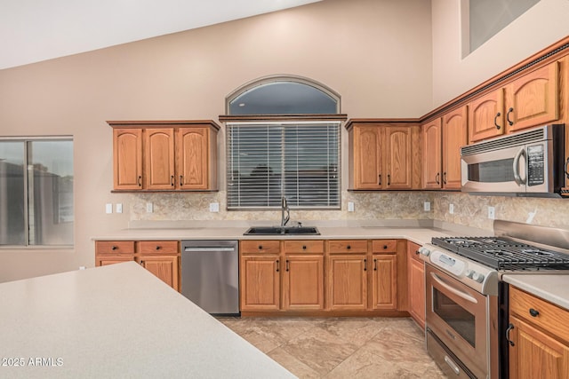 kitchen with high vaulted ceiling, light countertops, a sink, stainless steel appliances, and backsplash