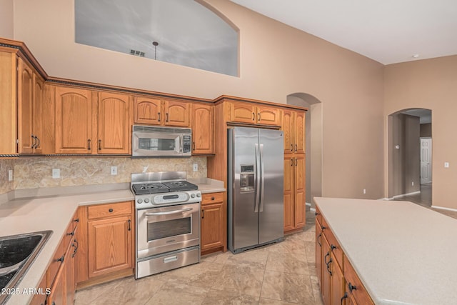 kitchen featuring tasteful backsplash, visible vents, brown cabinets, stainless steel appliances, and arched walkways