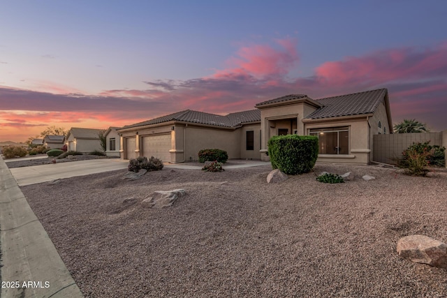 view of front facade featuring a tiled roof, an attached garage, fence, stucco siding, and driveway