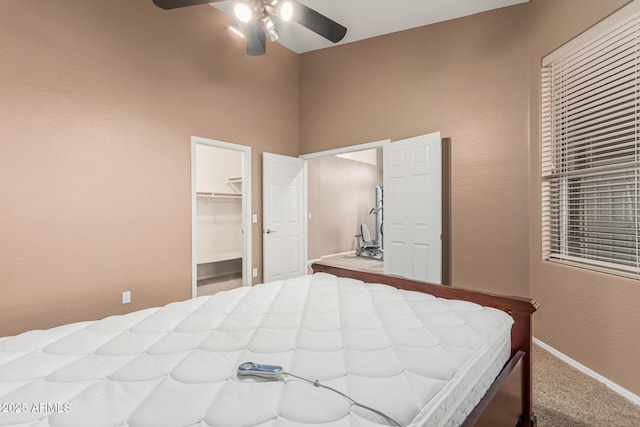 bedroom featuring baseboards, ceiling fan, carpet floors, a walk in closet, and a towering ceiling