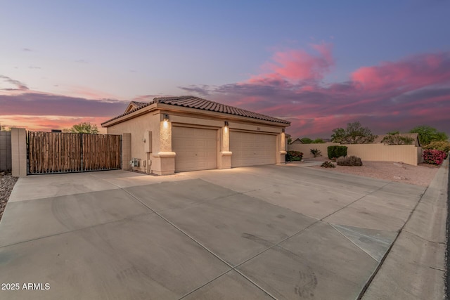view of front of house with concrete driveway, stucco siding, fence, a tiled roof, and a gate
