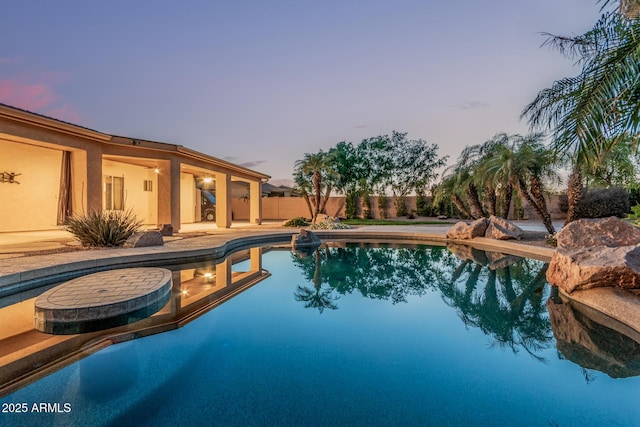 pool at dusk featuring a patio, a fenced backyard, and a fenced in pool